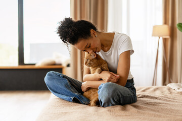 Young woman cuddling her ginger cat on bed at home