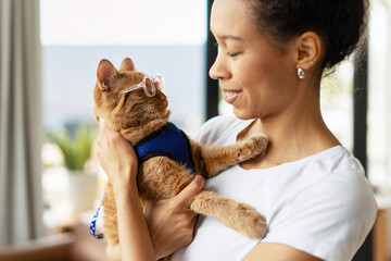 Veterinarian holding a ginger cat wearing eyeglasses and a harness