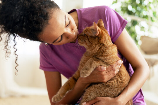 Young woman is kissing and hugging her ginger cat at home