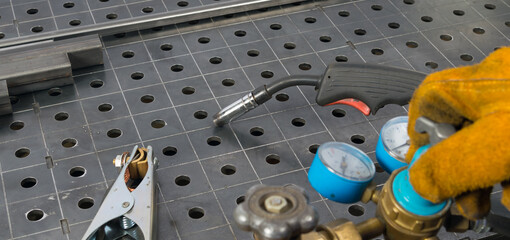 hand in protective glove opens gas cylinder for welding, against metal table background