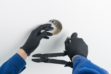 hands of a master in uniform in protective black gloves and with a tool, repairing electrical wiring lighting of a suspended ceiling