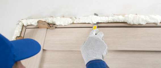 close-up, master in protective gloves and uniform, cuts the mounting foam of the doorway, after installation