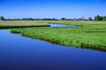 Authentic dutch river landscape with green meadows, water and blue sky, Netherlands.