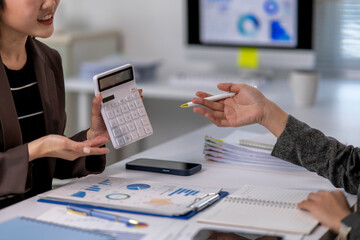 Businesswomen are using calculator and discussing charts at office desk