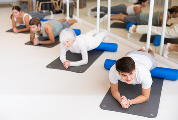 Sporty women and men practicing yoga positions during group training in fitness center, performing...