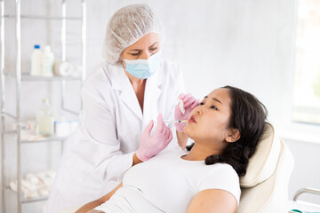 Closeup of professional cosmetologist hands in rubber gloves performing lips enhancement treatment...