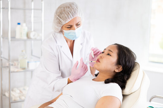 Closeup of professional cosmetologist hands in rubber gloves performing lips enhancement treatment to female client, making injection of lip fillers