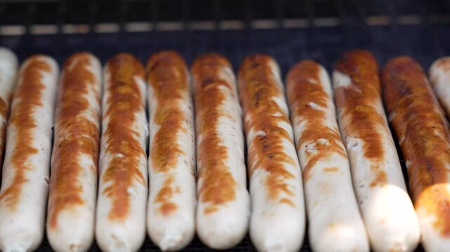 Bratwursts on the grill close-up. Juicy bratwursts lie in a perfect row on the grill. The even browning pattern makes you want to enjoy summer and BBQ.
