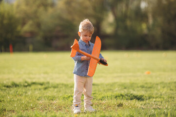 Fototapeta premium Orange colored toy plane is in hand. Little boy is having fun on the field outdoors