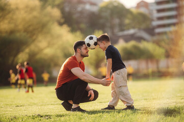 Keeping soccer ball by heads. Father and son are having fun outdoors