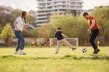 Running, playing soccer. Family of mother, father and son are playing on the field