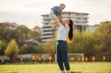 Up in the air, holding boy in hands. Mother and son are together on the summer field