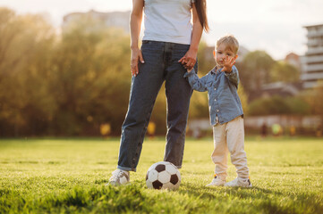 Active time spending with soccer ball. Mother and son are together on the summer field