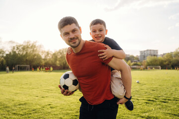 Ready to play soccer, boy is sitting. Father and son are having fun outdoors