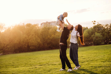 Holding kid in hands. Family of mother, father and son are playing on the field