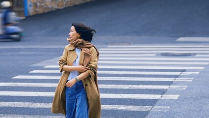 Woman crossing the street wearing a trench coat.