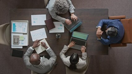 Top view of mature male sales manager sitting at table in meeting room while having meeting with diverse team members, discussing performance targets and studying reports - Powered by Adobe