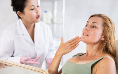 Woman beautician examining face skin of female patient before cosmetology procedure in beauty clinic