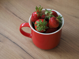Ripe garden strawberries in a red mug on the table. Wallpaper