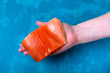Trout fillet piece in hand on turquoise wooden board. Fresh sea ingredient. Product selection, quality determination. Top view