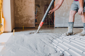 Construction worker pouring concrete surface flooring over underfloor heating system