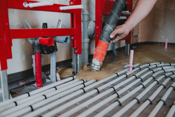 Construction worker pouring self-leveling concrete mix over underfloor heating system