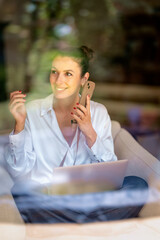 Attractiv middle aged woman sitting at home and using smart phone and laptop computer