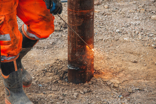 Close-up of welder using welding equipment to cut off steel pile on construction site creating fire arc of hot molten steel, sparks and smoke around