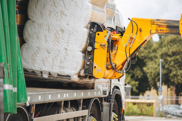 Telehandler forklift unloads large rolls of rockwool insulations from delivery truck at construction site