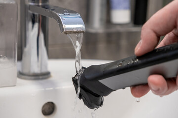 Hand rinsing electric shaver under flowing tap water, demonstrating essential daily grooming and...