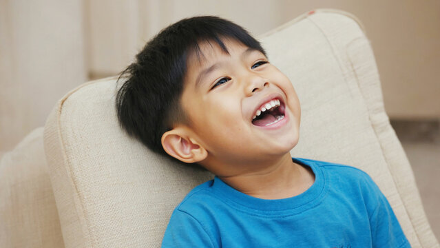 A young child sitting on a chair with a joyful expression, smiling at something