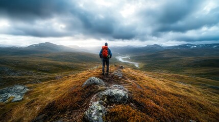 A lone hiker stands atop a rugged mountain peak, gazing over a vast, serene valley below, showcasing the beauty of nature amidst dramatic cloud formations and rugged terrain.