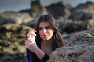 beautiful young woman dancing flamenco among the rocks by the seashore, wearing a purple velvet...