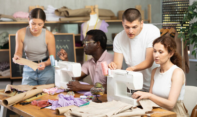 Kind young male teacher helping students sew while other drawing on paper during sewing class