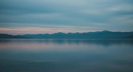 Obraz premium Calm water reflecting clear sky and soft mountain ridges on the horizon
