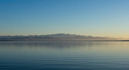 Fototapeta premium Serene reflective lake scene with distant mountain shadows in blue light