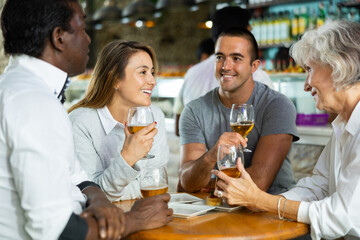 Spending time in bar. Four positive friends drinking beer in bar