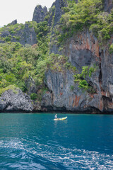 An Asian guy is paddling in the famous blue lagoon of El Nido with a beautiful backdrop of the magnificent limestone cliff. Palawan, Philippines is the favorite summer holiday in Asia