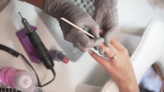 Close-up of a nail technician using a wooden stick to push back the cuticles during a manicure.