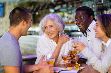 Friendly joyful family celebrating meeting holding glasses with beer in cosy bar. Main focus right in center