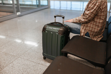 A partial view of a woman sitting in an airport terminal with a suitcase beside her. The scene...