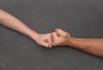 Male and female fists pressing against each other on neutral gray background, creating tension...
