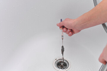 Person manually cleaning bathtub drain removing clog and dirt to restore water flow. Hand pulling...