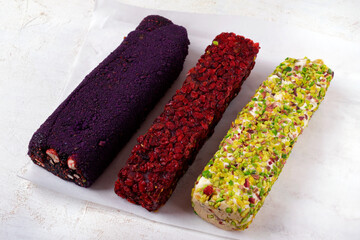 Turkish delight rolls with dried cranberries, pistachios, roasted hazelnuts and freeze dried berry powder. Three flavors of oriental sweetness on a white table