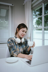 A young woman enjoys coffee and dessert while wearing headphones, working or studying remotely from...