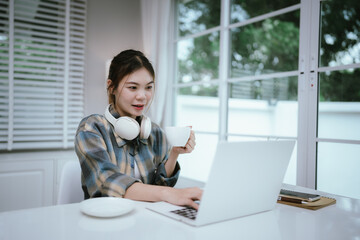 A young woman enjoys coffee and dessert while wearing headphones, working or studying remotely from...