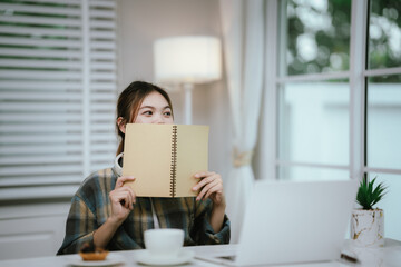 A young woman wearing headphones reads a book peacefully at home, enjoying a quiet study moment in...
