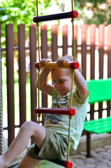 The little boy is playing in the yard, he is climbing the ladder.