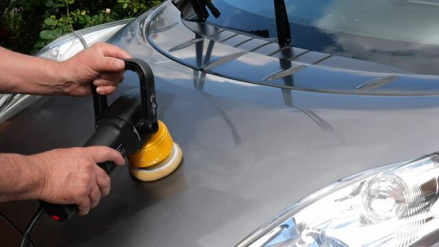 Closeup of a car hood being polished using rotary buffer . Well-lit clean workspace. Car maintenance car care with automotive cleaning, wax, shine, paint correction.