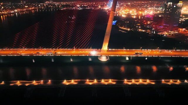 Nighttime aerial of tran thi ly bridge glowing over da nang, revealing urban landscape with streaming traffic against vibrant city lights